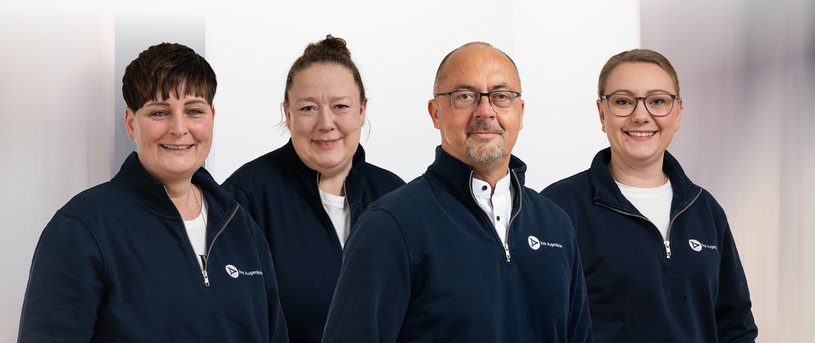 Vier lächelnde Personen in blauen Jacken mit Logo posieren für ein professionelles Gruppenfoto.