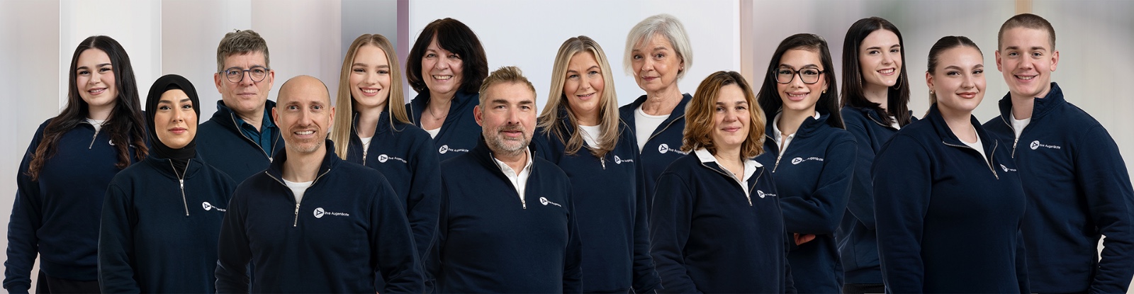 Gruppenfoto von 15 Personen in blauer Firmenkleidung, die freundlich in die Kamera lächeln.